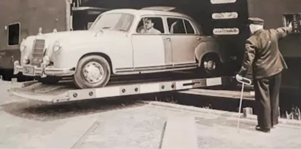 Historische Aufnahme von Arbeitern, die Autos auf einen Zug verladen